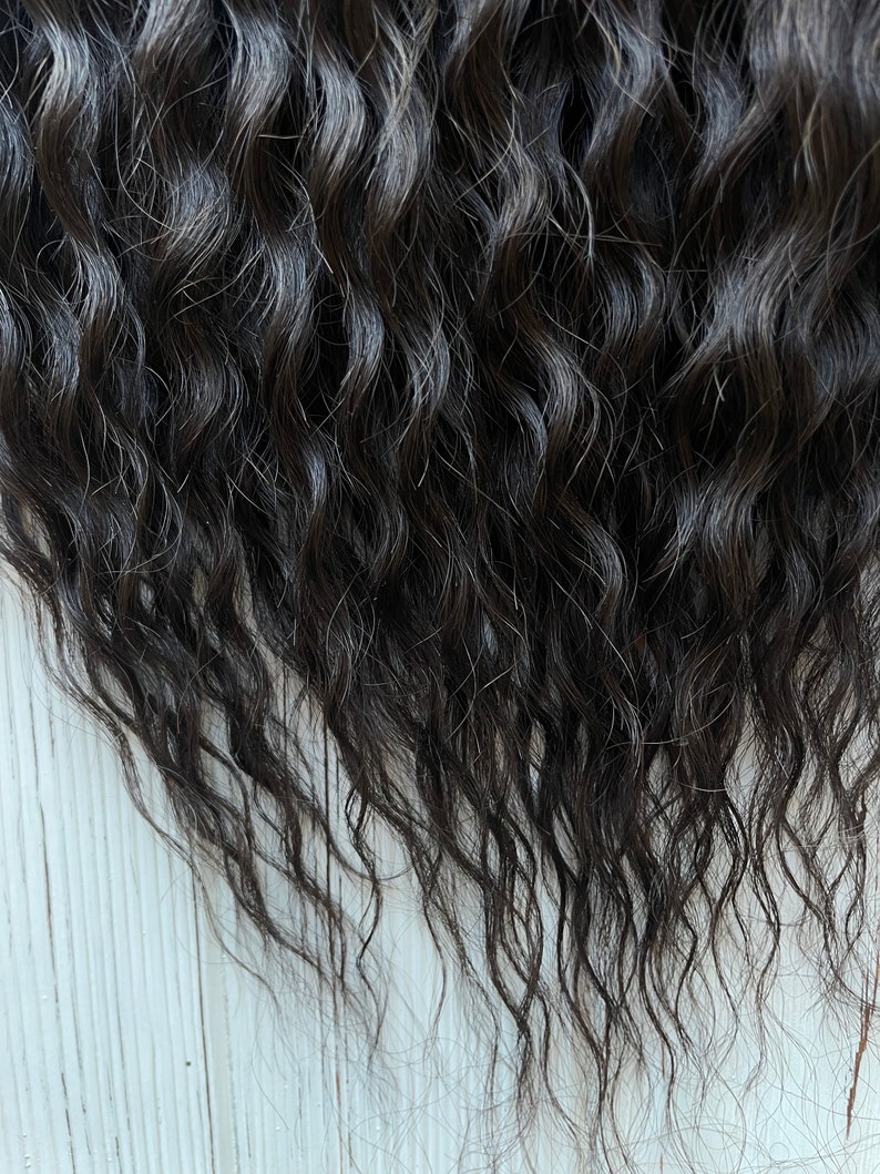 May include: Close-up of dark brown human hair extensions with a wavy texture.