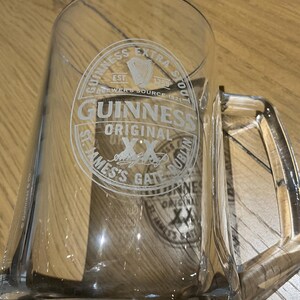 May include: A white ceramic mug with a black handle and the text "But First, Coffee" in a handwritten style. The mug is on a white surface. The mug is likely for hot beverages.