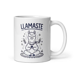 Op de afbeelding: Witte keramische mok met een marineblauwe illustratie van een mediterende lama. De tekst "LLAMASTE" staat boven de lama. De lama zit op een patroonkleed met gesloten ogen en handen in gebedshouding. Sterren en bladeren omringen de lama.