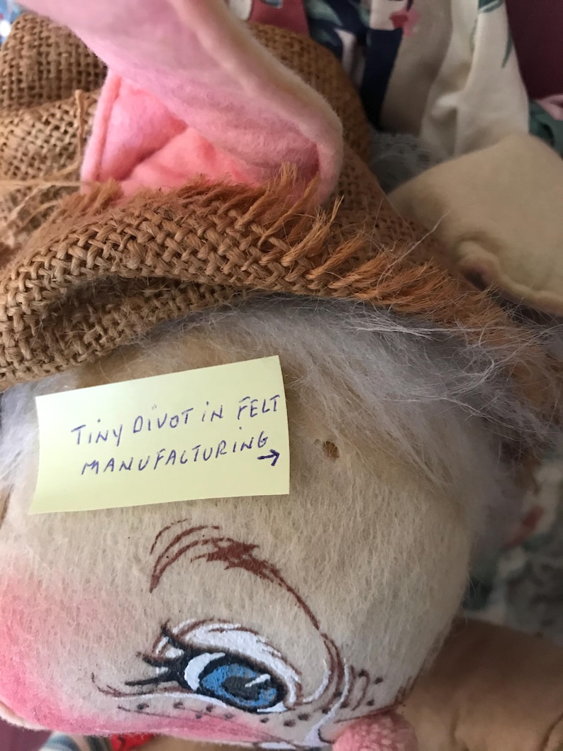 May include: A handmade plush bunny doll with a burlap hat and pink felt ears. The doll has painted facial features, including blue eyes and rosy cheeks. A yellow sticky note reads "Tiny divot in felt manufacturing."