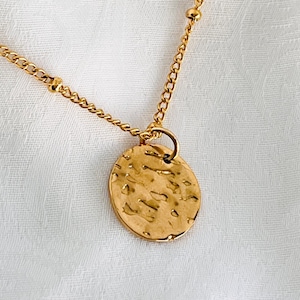 May include: A gold necklace with a hammered circle pendant and a chain with small beads.