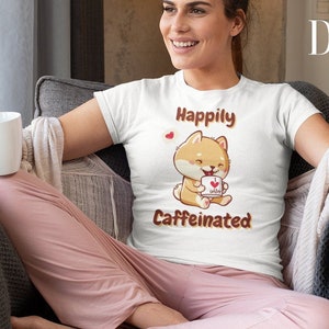 Op de afbeelding: Wit T-shirt met een cartoonhond die een kopje koffie vasthoudt en de tekst "Happily Caffeinated".
