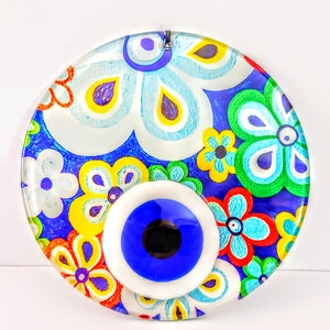 May include: A round glass ornament with a blue evil eye surrounded by colorful flowers. The evil eye is a symbol of protection against bad luck and envy.