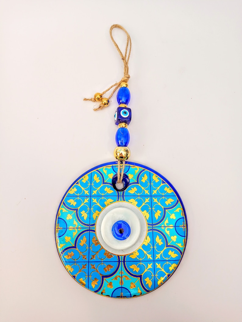 May include: A blue and gold ceramic wall hanging with a white evil eye design. The hanging has a string with blue and gold beads.