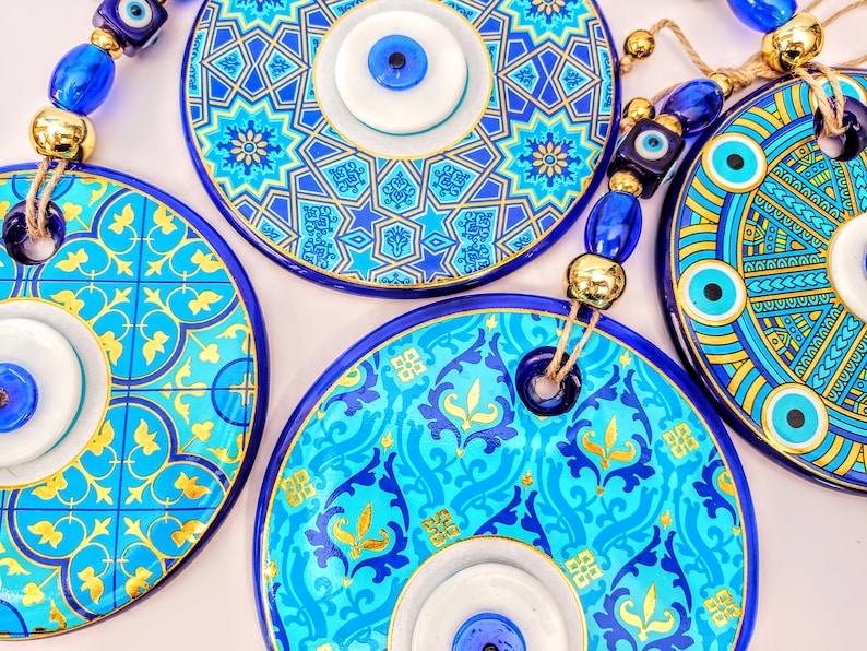 May include: Four blue and gold ceramic evil eye wall hangings with white and blue evil eyes. The evil eyes are strung together with blue and gold beads.