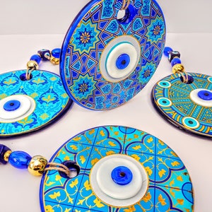 May include: Three blue and gold ceramic wall hangings with evil eye charms. Each hanging features a different geometric pattern and a white evil eye with a blue center.