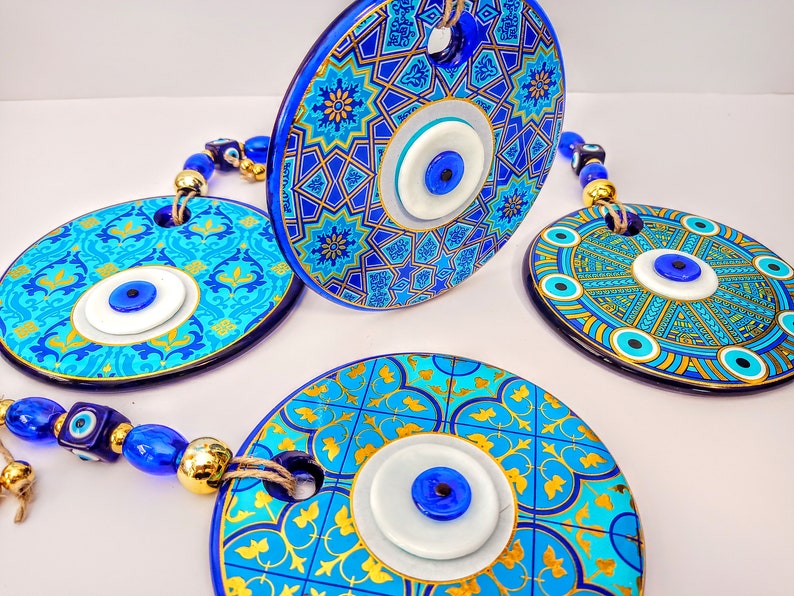 May include: Three blue and gold ceramic wall hangings with evil eye charms. Each hanging features a different geometric pattern and a white evil eye with a blue center.