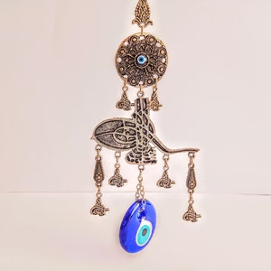 May include: A silver and blue evil eye wall hanging with a decorative design. The hanging features a large blue evil eye charm and a smaller evil eye charm in a circular design.