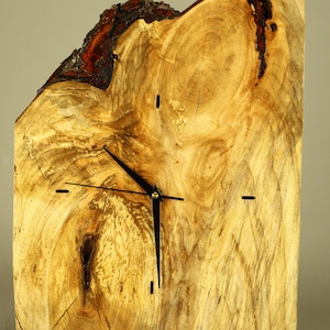 May include: A unique wooden clock with a natural edge. The clock face is made from a cross-section of a tree trunk, showcasing the wood's grain and knots. Black clock hands and minimalist hour markers complete the design.