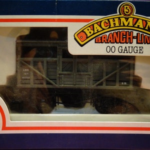 May include: A Bachmann Branch-Line OO Gauge model train box featuring a gray and brown freight car. The box has a red, white, and blue border and a red and white logo with the text "Bachmann Quality Since 1833".