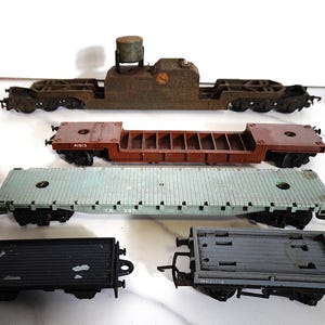 May include: A selection of vintage model railway wagons in different colours. The wagons include a brown tank wagon, a red flatbed wagon, a green flatbed wagon, a black flatbed wagon, and a grey flatbed wagon. These model railway wagons are designed for a model railway set.