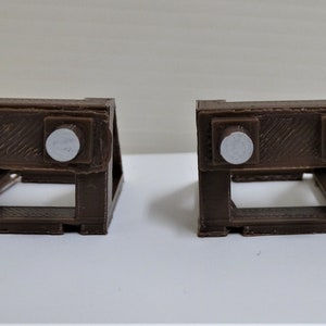 May include: Two brown plastic stands with white circles on top. The stands are designed to hold objects in place.