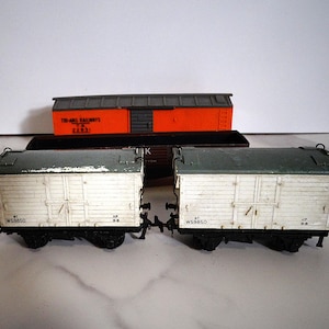May include: Three model railway wagons. Two white and grey box wagons are in the foreground, with a red and grey wagon behind. The box wagons have the number W58550 printed on them.