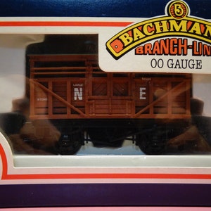 May include: A brown wooden boxcar model train car with black wheels and the letters "N E" on the side. The boxcar is labeled "Bachmann Branch-Line OO Gauge".