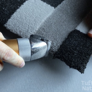 May include: A close-up of a hand using a handheld electric fabric shear to trim the edges of a black and white striped rug.