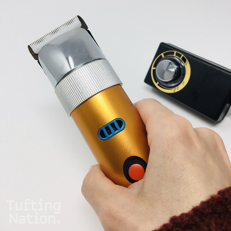 May include: A gold electric hair clipper with a silver blade and a blue and black power button. The clipper is being held in a hand.
