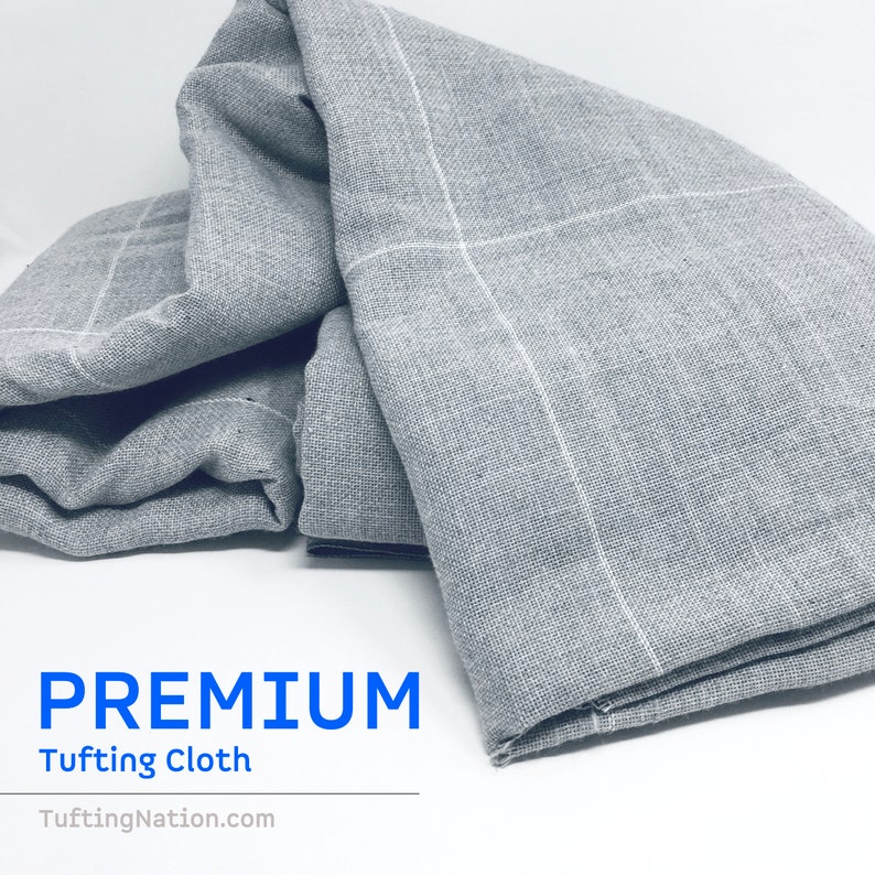 K&ouml;nnte beinhalten: Nahaufnahme eines grauen, strukturierten Stoffes mit wei&szlig;en Gitterlinien. Der Stoff ist gefaltet und wirkt weich. Der Text "PREMIUM Tufted Cloth TuftedNation.com" ist unter dem Stoff gedruckt.