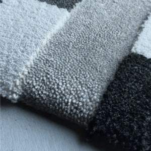 May include: Close-up of a gray and black tufted rug with a geometric pattern. The rug is made of soft, plush fibers and has a subtle sheen.