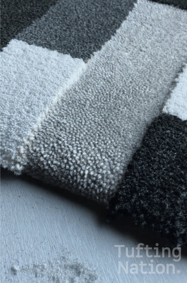 May include: Close-up of a gray and black tufted rug with a geometric pattern. The rug is made of soft, plush fibers and has a subtle sheen.