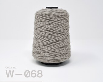 May include: A spool of light gray yarn with the color number W-068. The yarn is wound tightly on the spool and is ready for use in crafting projects.