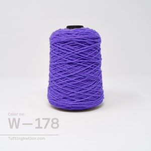 May include: A spool of purple yarn with the colour number W-178. The yarn is wound tightly and has a smooth texture.
