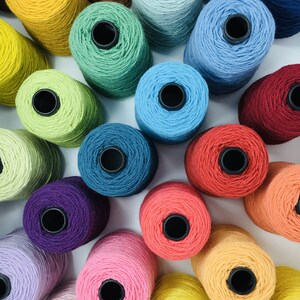 May include: A collection of colorful yarn spools in various shades of blue, green, red, yellow, orange, pink, and purple. The spools are arranged in a circular pattern on a white surface.