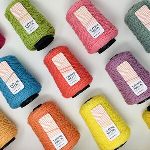 May include: A collection of 10 spools of yarn in various colors, including yellow, orange, red, pink, purple, blue, green, and brown. Each spool has a label that reads "Tufting Nation."