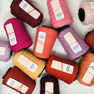 May include: A collection of colorful yarn spools labeled "Tufting Nation." The spools are arranged in a circular pattern on a white surface. The yarn is 100% wool.
