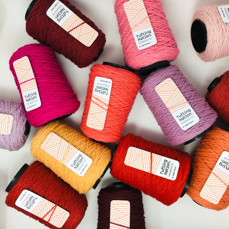 May include: A collection of colorful yarn spools labeled "Tufting Nation." The spools are arranged in a circular pattern on a white surface. The yarn is 100% wool.