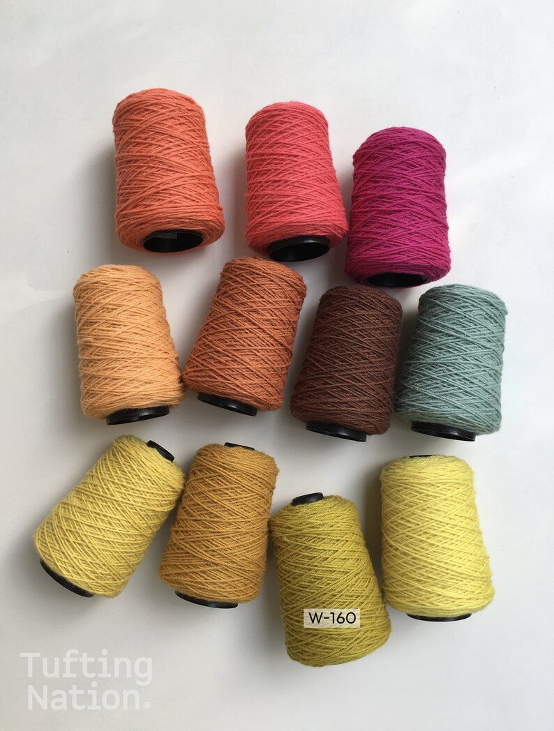 May include: Ten spools of yarn in various shades of orange, brown, yellow, and green. The spools are arranged in a circle on a white surface. The text "W-160" is visible on one of the spools.