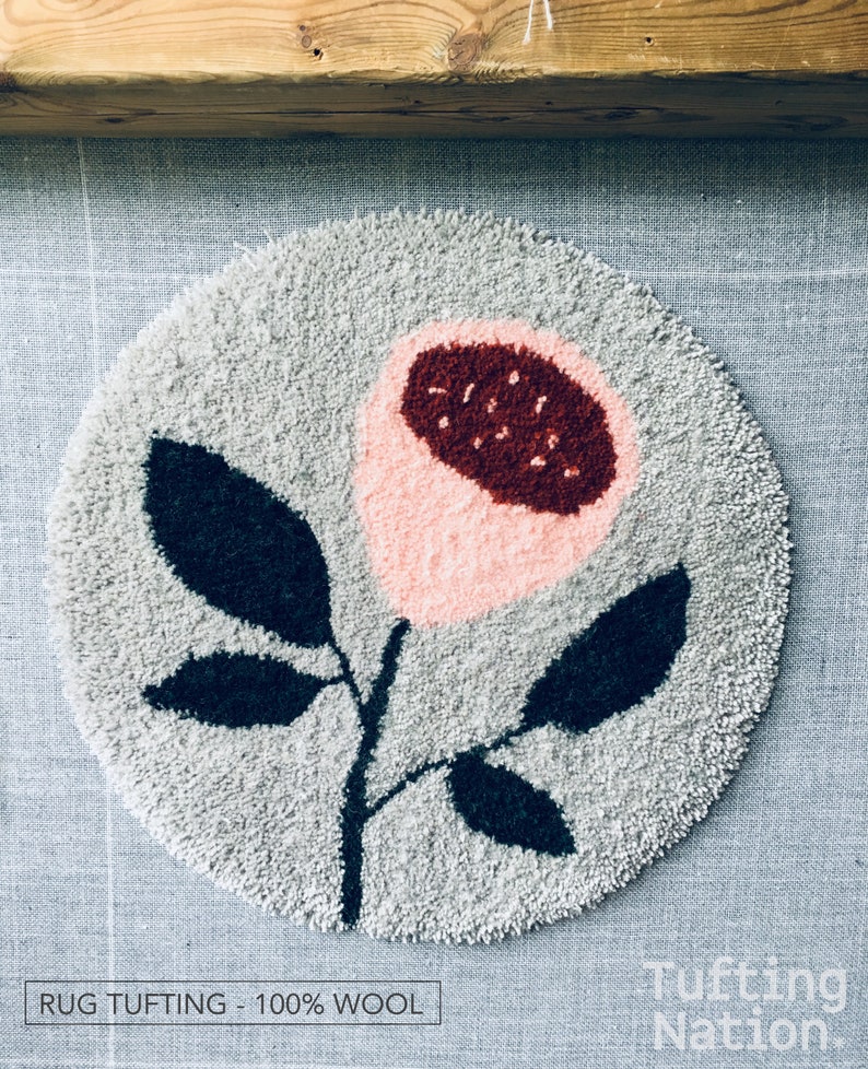 May include: A round, gray rug with a pink and red flower design. The rug is made of 100% wool and is tufted. The text "RUG TUFTING - 100% WOOL" is visible at the bottom of the image. The text "Tufting Nation" is visible at the bottom right of the image.