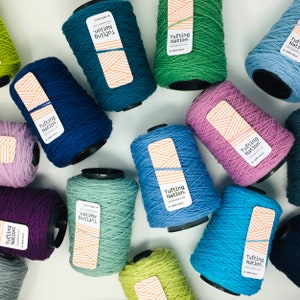 K&ouml;nnte beinhalten: Sortiment an bunten Garnrollen mit der Aufschrift "Tufting Nation". Das Garn ist 100% Wolle und in verschiedenen Farben erh&auml;ltlich, darunter Gr&uuml;n, Blau, Lila und Rosa.