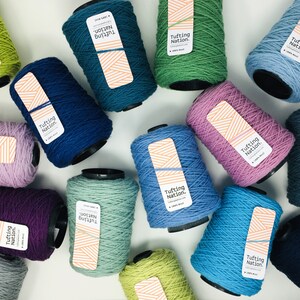 May include: Assortment of colorful yarn spools labeled "Tufting Nation." The yarn is 100% wool and is available in a variety of colors, including green, blue, purple, and pink.