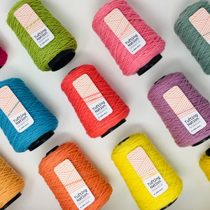 May include: A collection of 10 spools of yarn in various colors, including yellow, orange, red, pink, purple, blue, green, and brown. Each spool has a label that reads "Tufting Nation."