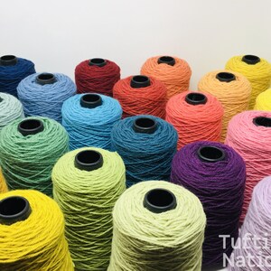 May include: A collection of colorful yarn spools in various shades of blue, green, yellow, orange, red, pink, and purple. The spools are arranged in a semi-circle, with the ends of the yarn spilling out.