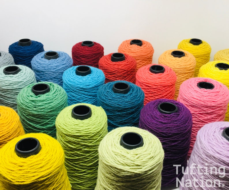 May include: A collection of colorful yarn spools in various shades of blue, green, yellow, orange, red, pink, and purple. The spools are arranged in a semi-circle, with the ends of the yarn spilling out.