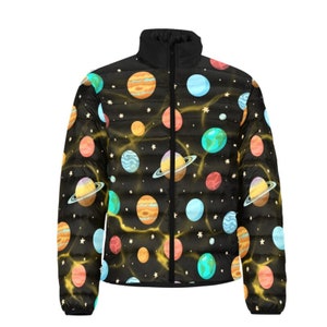 Puede incluir: Chaqueta acolchada negra con un colorido diseño de planetas y estrellas. La chaqueta tiene un cuello alto y una cremallera completa. Los planetas son en tonos naranja, azul, amarillo y verde, sobre un fondo negro con estrellas blancas y líneas amarillas.