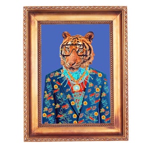 May include: A framed art print depicting a tiger in a blue floral suit, glasses, and jewellery. The artwork is set against a blue backdrop within a gold-coloured frame. The image presents a quirky and fashionable portrait.