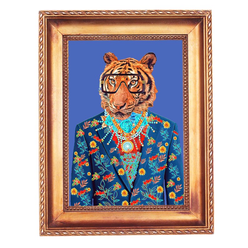 May include: A framed art print depicting a tiger in a blue floral suit, glasses, and jewellery. The artwork is set against a blue backdrop within a gold-coloured frame. The image presents a quirky and fashionable portrait.