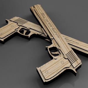 May include: Two wooden toy guns with a light wood grain finish and black edges are displayed against a grey background. One gun is positioned on top of the other. Text is visible on the top gun.
