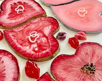 May include: Set of pink and red heart-shaped resin coasters with gold trim. Some coasters have glitter and a flower design.