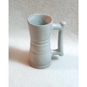 May include: A white ceramic mug with a handle. The mug has a slightly flared top and a rounded bottom. It has a simple design with three horizontal lines around the middle.