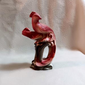 May include: A ceramic figurine of a red and white bird with a long tail, perched on a brown branch.
