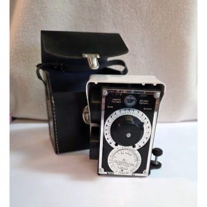 May include: A vintage black and white Hopkins Mfg. Corp. instrument with a leather case. The instrument has dials, a knob, and the text "ABOVE TARGET" and "BELOW TARGET". The case is open, revealing the instrument.