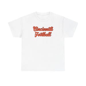 Puede incluir: Una camiseta blanca con la frase "Cincinnati Football" en escritura naranja. El texto tiene un diseño retro con un contorno naranja más oscuro. La camiseta está hecha de un material suave y cómodo.