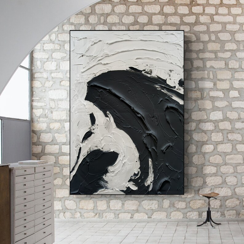 May include: Abstract painting with black and white paint strokes. The painting is on a canvas and is framed. The painting is hanging on a brick wall.