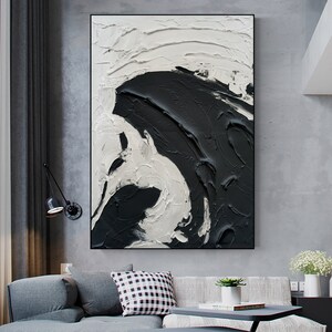 May include: Abstract painting with black and white paint in a thick, textured style. The painting is framed and hanging on a wall.