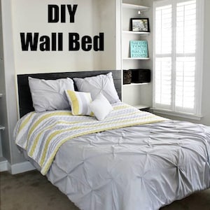 May include: A DIY wall bed with a gray and white striped bedspread and a gray comforter. The bed has a black headboard and is in a bedroom with white walls and a ceiling fan.