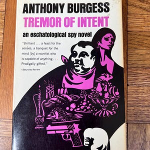 May include: Vintage paperback book cover for "Tremor of Intent" by Anthony Burgess. The cover has a black background with pink and white illustrations, including a man, woman, and a gun. Text includes the title and author.