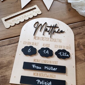 May include: A wooden sign with the name "Matthes" in black script, designed for a child's first day of school. It includes details like age, class, height (1.25m), teacher's name, and career aspiration.